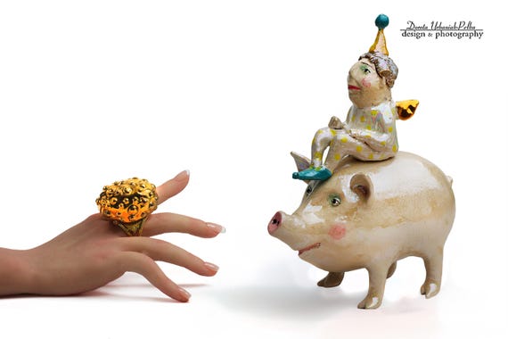 A one-of-a-kind ceramic angel riding a galloping pig — absurdist folk-art energy that is genuinely impossible to ignore.