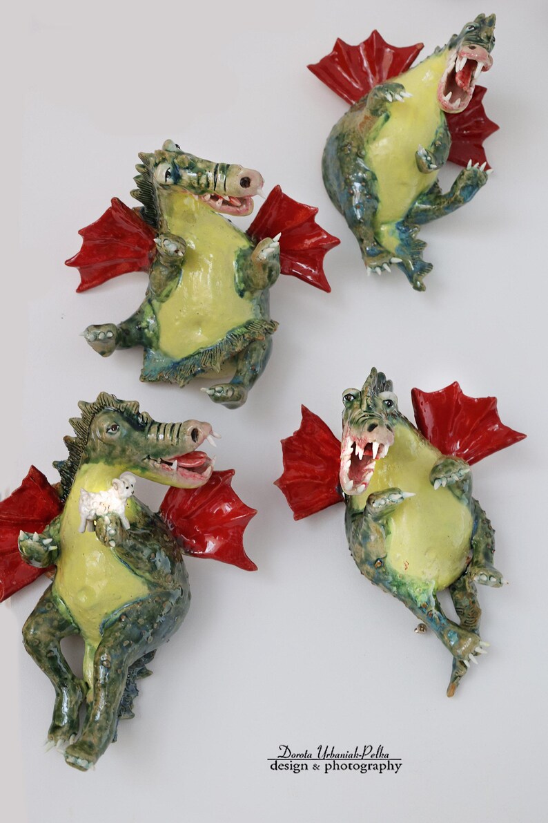 Pu&ograve; includere: Quattro figurine di draghi in ceramica con ali rosse, pance gialle e dettagli verdi e blu. Un drago tiene in mano un piccolo agnello bianco. I draghi hanno la bocca aperta e sono in varie pose.