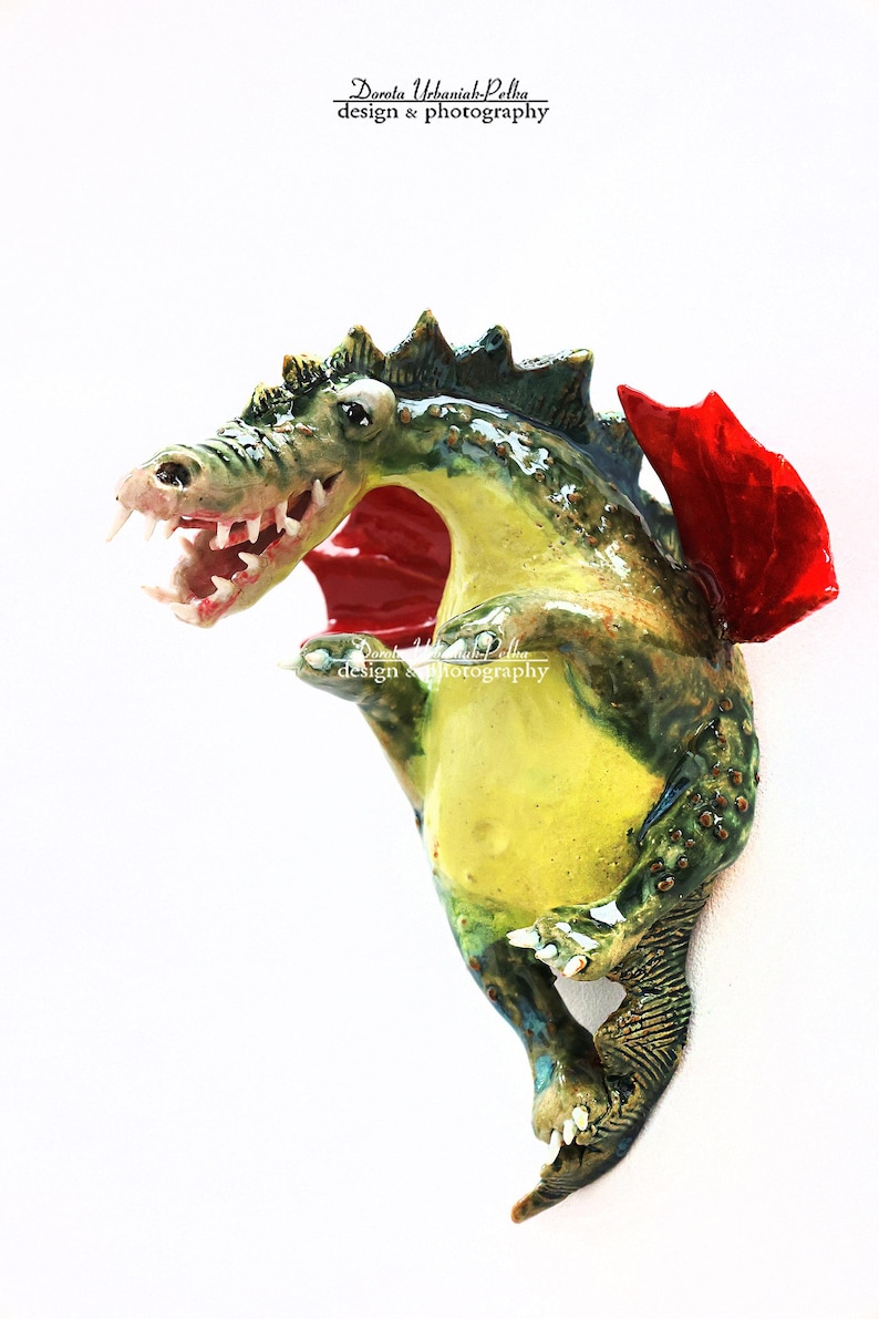 Pu&ograve; includere: Scultura di drago in ceramica fatta a mano nei toni del verde, giallo e blu, con un'ala rossa. Il drago ha la bocca aperta con denti visibili. La scultura &egrave; firmata "Dorota Urbaniak-Pelka design & photography".
