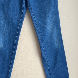 Op de afbeelding: Close-up van een blauwe spijkerbroek. De jeans heeft een klassieke rechte pijp en is gemaakt van een medium-wash denim stof. De afbeelding toont de voorkant van de jeans, met de naden en details van de stof duidelijk zichtbaar.