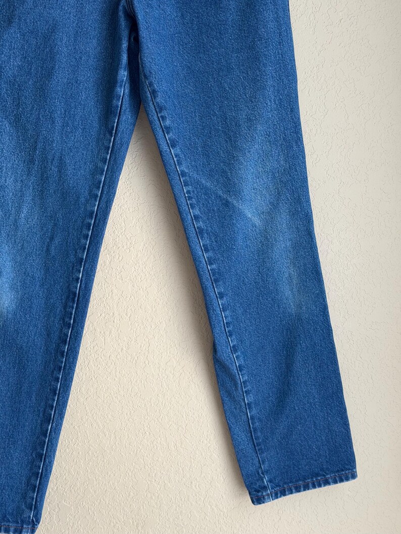 Op de afbeelding: Close-up van een blauwe spijkerbroek. De jeans heeft een klassieke rechte pijp en is gemaakt van een medium-wash denim stof. De afbeelding toont de voorkant van de jeans, met de naden en details van de stof duidelijk zichtbaar.