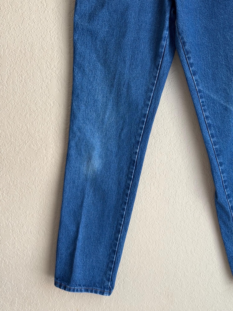 Op de afbeelding: Close-up van een blauwe spijkerbroek. De jeans heeft een medium wassing met een rechte pijp. Er is een lichte verkleuring op het linkerbeen. De jeans is gemaakt van een duurzame denim stof.
