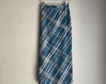 May include: A long, teal skirt with a plaid pattern of white and dark blue lines. The skirt is hanging on a white hanger against a plain wall. The skirt appears to be made of a lightweight fabric.