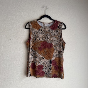 May include: A sleeveless top featuring a complex pattern of deep red roses, golden-brown textured sections, and intricate black and white filigree-style scrollwork. The garment has a round neckline and is displayed on a black plastic hanger.