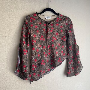 May include: A brown and black long-sleeved shirt with a red rose and leopard print pattern. The shirt has a ruffled hem and bell sleeves. The shirt has a label that reads "Amy Byer".