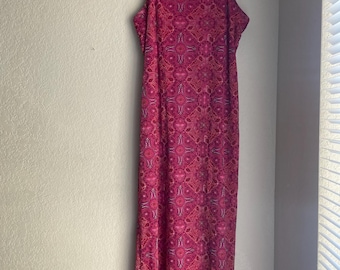 May include: A long, sleeveless dress in shades of pink and magenta, hanging on a black hanger. The dress features a repeating floral pattern and thin spaghetti straps. The dress is made of a lightweight material.