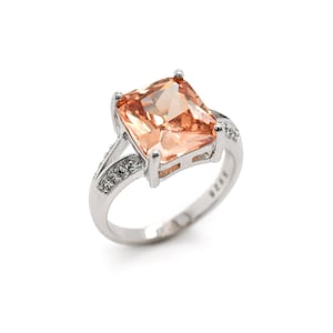May include: A silver ring with a large, square-shaped, peach-colored gemstone. The ring is set with smaller, clear gemstones around the band.