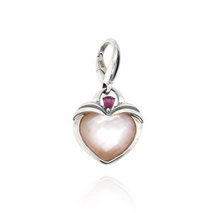 May include: A heart-shaped pendant with a pearlescent center and a silver-colored frame. A small, red gemstone sits above the heart. The pendant has a clasp for attaching to a necklace or bracelet. The jewelry is set against a white background.