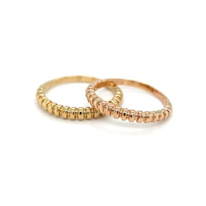 May include: Two thin gold rings with a beaded texture. One ring is yellow gold and the other is rose gold.