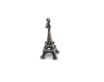 May include: A silver charm in the shape of the Eiffel Tower. The charm is detailed and has a green stone at the top.