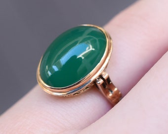 May include: A gold ring with a large oval green gemstone set in a bezel setting.