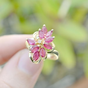 以下が含まれることがあります： 花の形にセットされたピンクのルビーの石のクラスターが付いた金のリング
