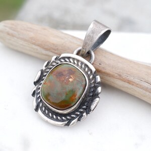 May include: A silver pendant with a green and brown stone set in a silver frame. The pendant has a rope-like design around the edge of the frame.