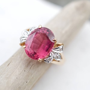 Puede incluir: Un anillo de oro con una piedra ovalada rosa y detalles de diamantes.