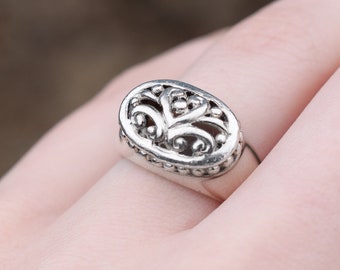 May include: A silver ring with an oval-shaped design featuring a delicate, intricate filigree pattern. The ring is worn on a finger.