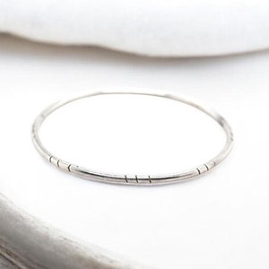 May include: A thin silver bangle bracelet with a textured design.