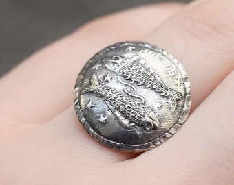 May include: A silver ring with a round design featuring two fish. The fish are detailed with scales and fins.
