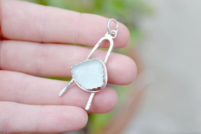 May include: A silver pendant featuring a light blue piece of sea glass set in a silver frame. The pendant is suspended from a silver bail.