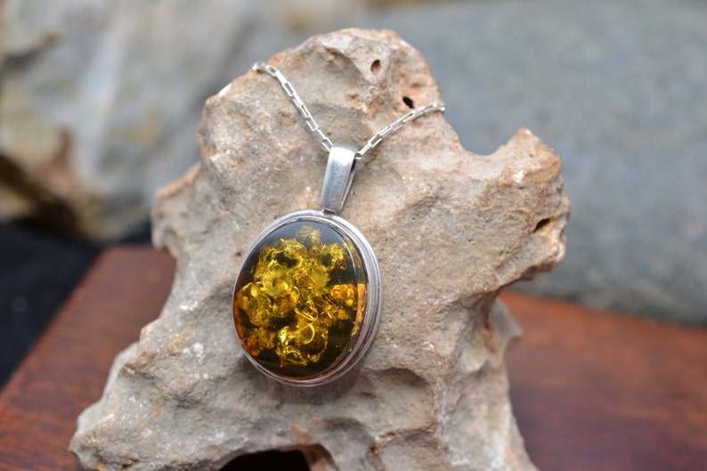 May include: A silver pendant necklace with a large oval amber stone. The amber is a deep yellow color and has a lot of inclusions. The pendant is on a silver chain.