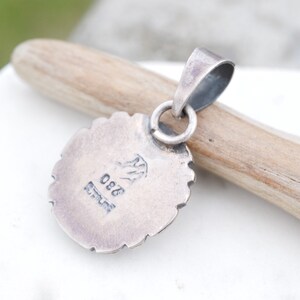 May include: Silver pendant with a detailed design and a stamped mark on the back that reads "925 Sterling".