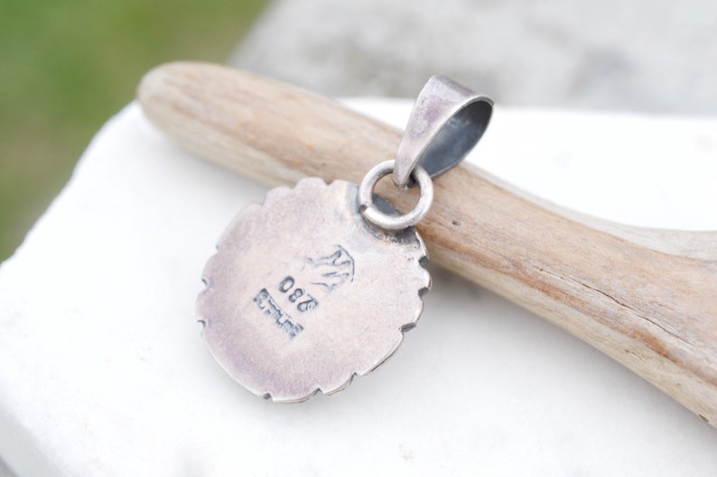 May include: Silver pendant with a detailed design and a stamped mark on the back that reads "925 Sterling".