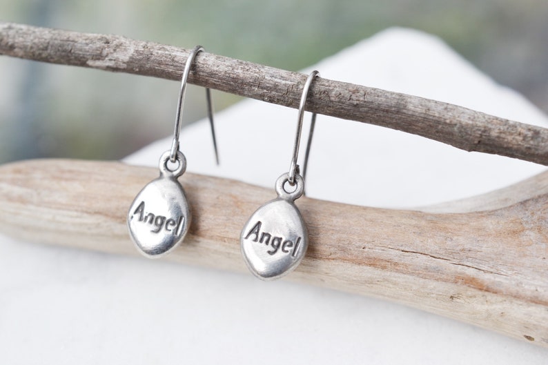 Puede incluir: Un par de pendientes de aro de plata con la palabra "Angel" grabada en cada dije.