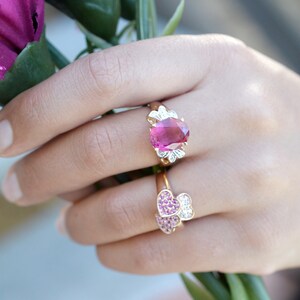 May include: Two rings with pink gemstones. The top ring features a large oval-shaped pink gemstone surrounded by smaller white gemstones. The bottom ring features two heart-shaped pink gemstones.