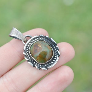 May include: A silver pendant with a green and brown oval stone set in a decorative silver frame.