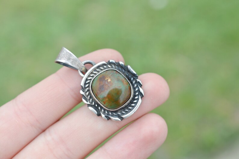 May include: A silver pendant with a green and brown oval stone set in a decorative silver frame.