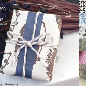 May include: A gift wrapped in brown paper with a white and blue striped ribbon. The paper has a brown print of a repeated design. The gift is tied with twine and a bow. The text "Custom Gift Wrap" and "Add at Checkout" is visible in the image. The image also shows a variety of other gift wrap patterns.