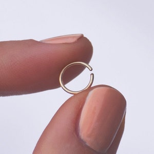 K&ouml;nnte beinhalten: Ein goldener Nasenring, gehalten zwischen zwei Fingern.