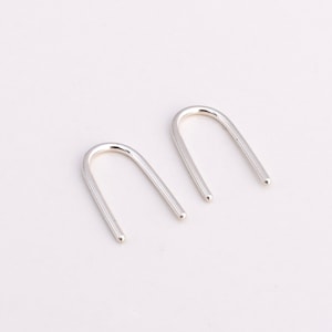 May include: A pair of silver minimalist earrings in the shape of an arch.
