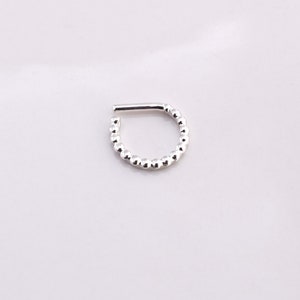 Puede incluir: Un aro de nariz plateado con cuentas y una abertura con bisagra.