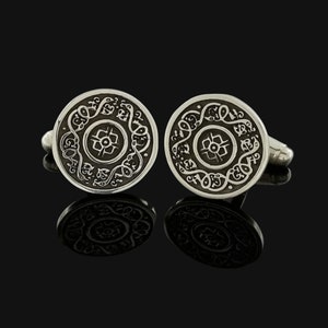 May include: A pair of silver cufflinks with a circular design featuring intricate black filigree and a central motif.