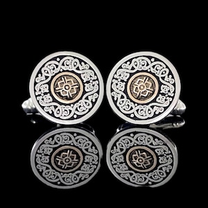 May include: A pair of silver cufflinks with a black and gold design. The cufflinks feature a circular design with intricate details.