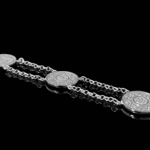 May include: Silver chain bracelet with three round, decorative charms. The charms have a detailed, intricate design.