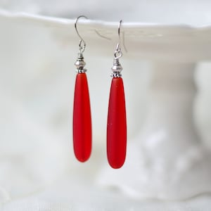 May include: A pair of red glass teardrop earrings with silver bead accents.