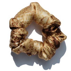 May include: A brown and beige patterned scrunchie made of satin fabric.