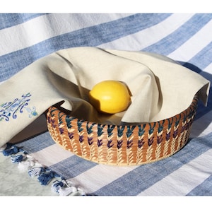 May include: A woven basket with a blue and purple design sits on a white and blue striped tablecloth. A yellow lemon is inside the basket.