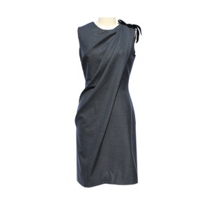 Puede incluir: Un vestido gris sin mangas con un diseño drapeado y un detalle de lazo negro en el hombro.