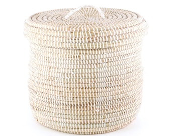 May include: A round, natural woven storage basket with a white lid and a white handle. The basket is made of natural materials and has a natural, rustic look.
