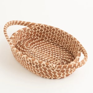 May include: A woven oval basket with two handles. The basket is made of natural materials and has a light brown color.