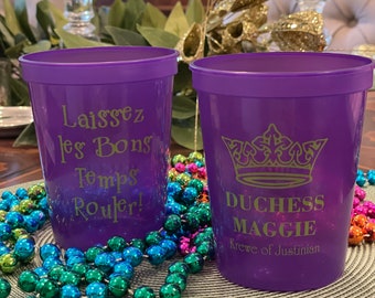 May include: Two purple plastic cups with gold lettering. The cup on the left says "Laissez les Bons Temps Rouler!" The cup on the right says "Duchess Maggie Krewe of Justinian" with a gold crown above the text.