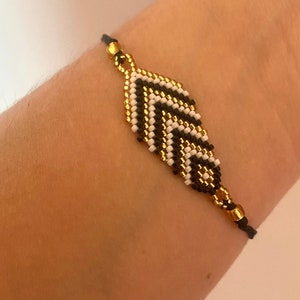 Könnte beinhalten: Ein Armband aus schwarzen und weißen Perlen mit einem goldenen Blattdesign. Das Armband ist verstellbar und hat eine schwarze Schnur.