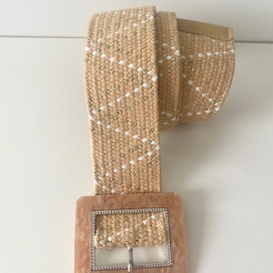 May include: A beige woven belt with a white and gold pattern and a large, square, light brown buckle.