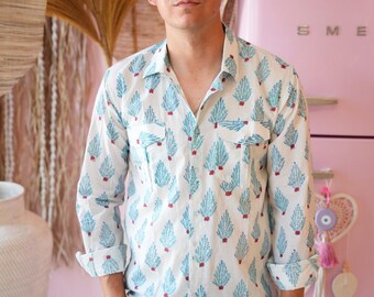 May include: White button-down shirt with a blue and red pattern. The long-sleeved shirt has two chest pockets and is paired with blue jeans. The shirt's pattern features a repeating design of blue leaf-like shapes with red accents.