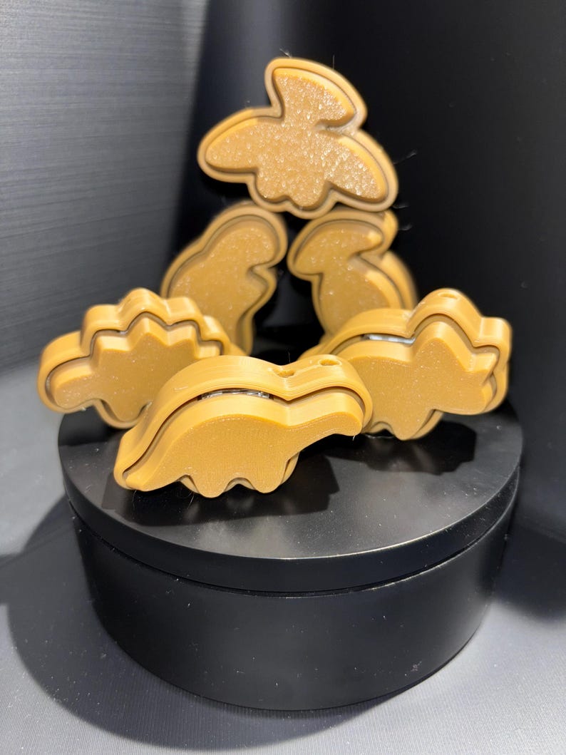 May include: A set of five brown dinosaur-shaped cookie cutters. The cutters are made of a smooth, shiny plastic and are arranged in a pyramid shape.