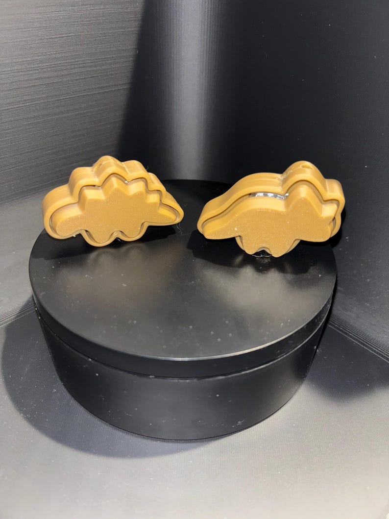 May include: Two brown dinosaur-shaped cookie cutters. The cutters are made of a smooth, shiny plastic.