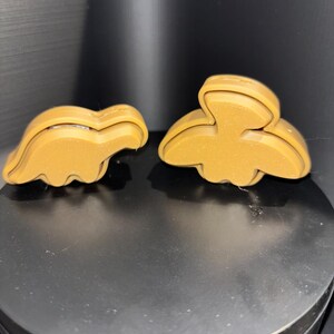 May include: Two brown cookie cutters, one shaped like a dinosaur and the other shaped like a bird.
