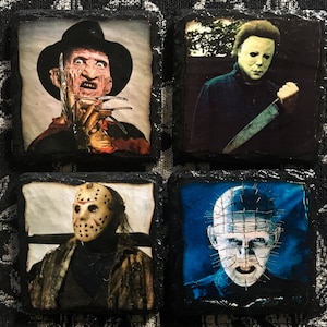 May include: Four square black slate coasters with images of horror movie characters. The coasters feature Freddy Krueger, Michael Myers, Jason Voorhees, and Pinhead.